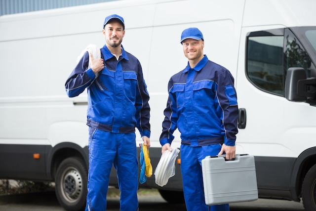 Smiling plumber With Toolbox And Cable Standing In Front Of Vehicle