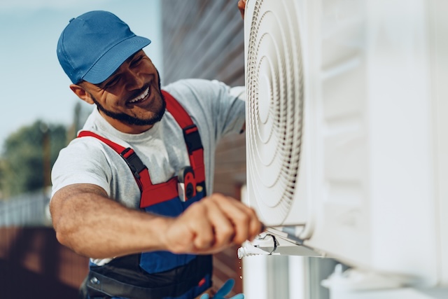 Young black man repairman checking an outside air conditioner unit close up after being hired through his home services marketing