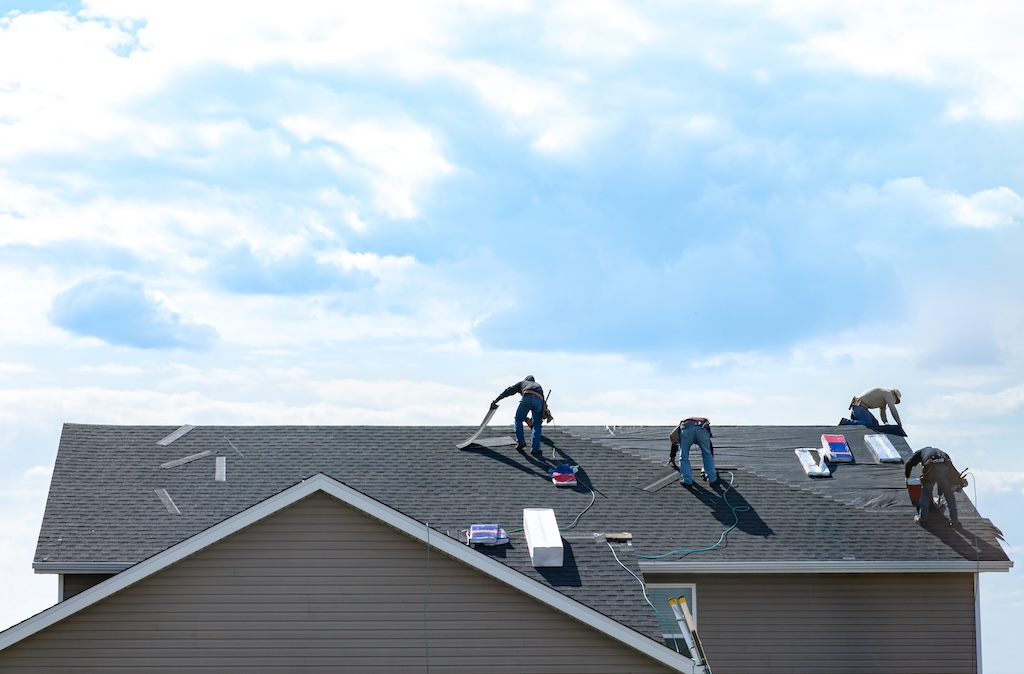 4 construction workers fixing roof against clouds blue sky, install shingles at the top of the house after getting job through roofing marketing. 