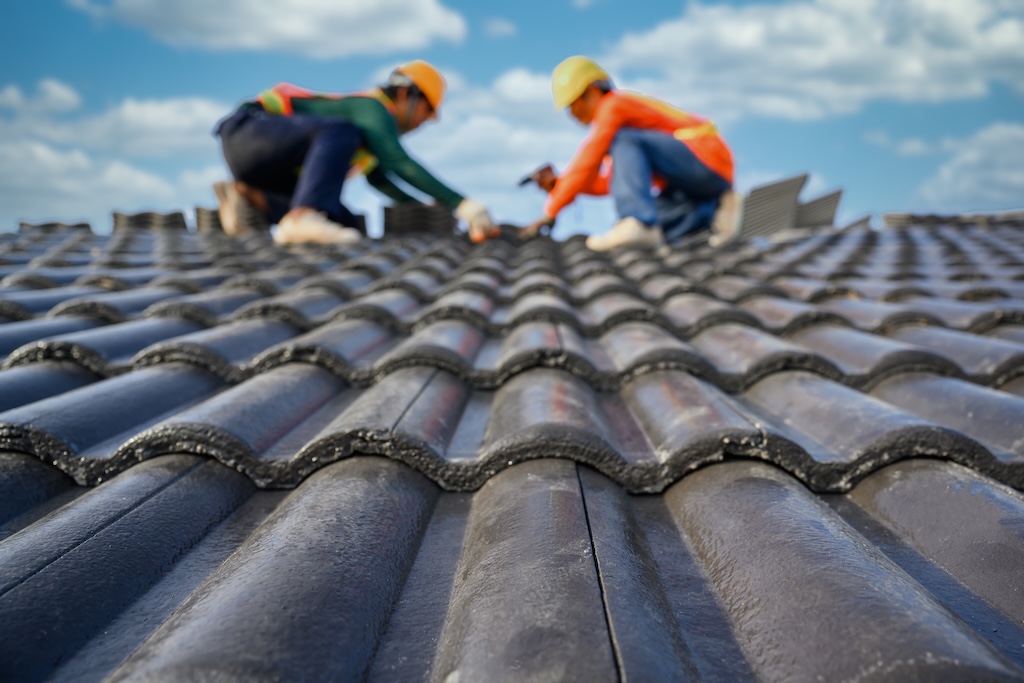 Blurred background of a roofer working on the roof of a house using a drill to drill the screws to fix the cement tiles.